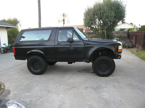1986 Ford Bronco - A modified SUV with a lifted suspension and large tires sits on a concrete driveway.