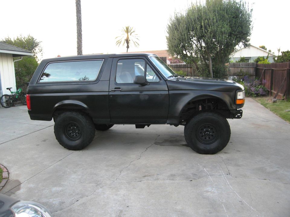 Lifted black SUV parked on a driveway. It has large off-road tires and a matte black finish