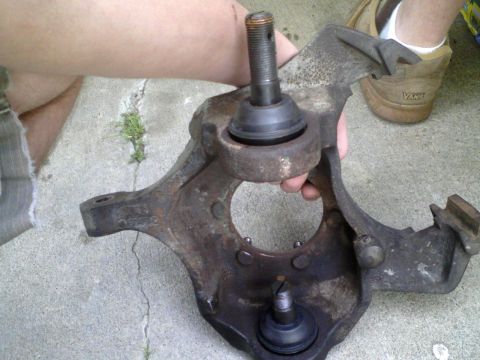 1986 Ford Bronco - A close-up of a rusty suspension knuckle with ball joints, held by a person.