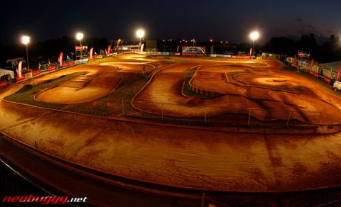 1986 Ford Bronco - A dirt RC car race track is lit up by floodlights at night, with various jumps and turns visible.