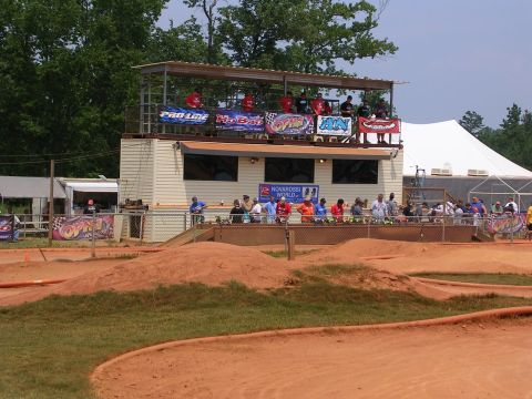 1986 Ford Bronco - Spectators and racers gather at an outdoor RC car track, with a building providing elevated viewing and shelter.