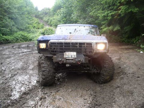 1979 Ford Bronco - A heavily muddied 1978 Ford Bronco navigates a treacherous dirt path through a wooded area.