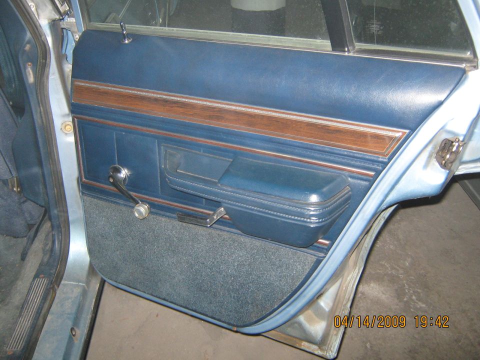 Blue vinyl door panel with wood trim, armrest, and crank window handle