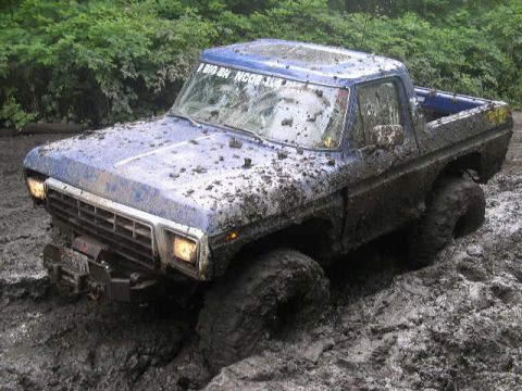 1979 Ford Bronco - This blue 1979 Ford Bronco is heavily covered in mud, with its front end partially submerged in a muddy terrain.