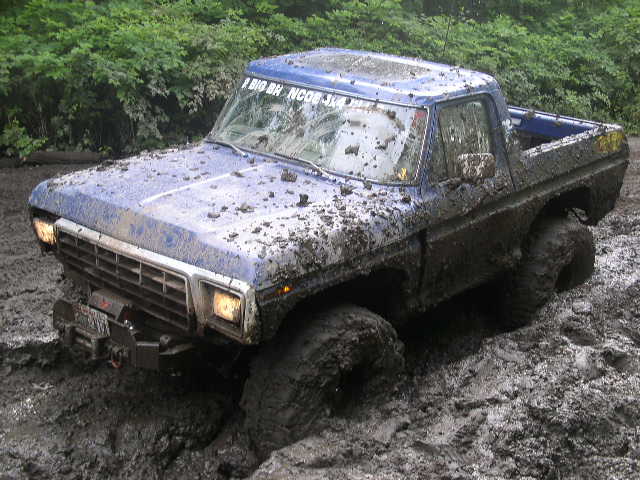 Muddy blue 1970s Ford pickup buried to the axles in a mud pit