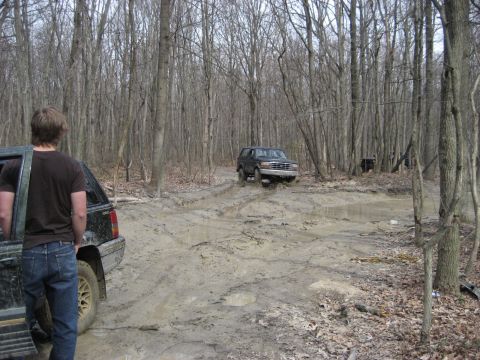 1991 Ford Bronco - A dark Ford Bronco navigates a muddy trail in a wooded area.