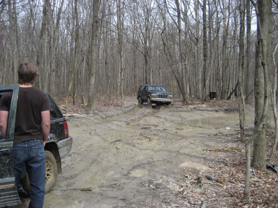 Dark Ford Bronco driving through mud, front grille visible