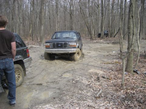 1991 Ford Bronco - A 1991 Ford Bronco navigates a muddy off-road course with another vehicle visible in the background.