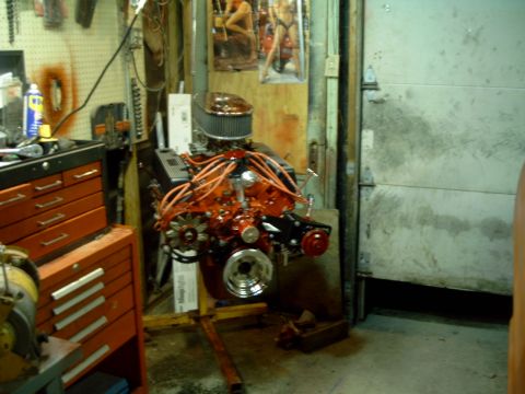 1967 Ford Galaxie - A V8 engine is displayed on a stand in a cluttered garage setting.