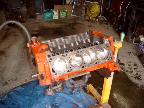 1967 Ford Galaxie - An orange V8 engine block, likely undergoing repair or rebuild, is shown on a stand in a cluttered garage setting.