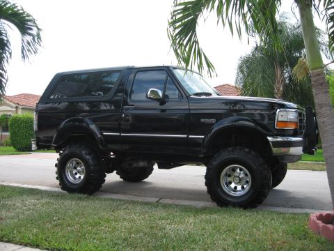 1994 Ford Bronco - This lifted black 1994 Ford Bronco is parked in front of a house with palm trees in the background.