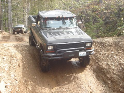 1989 Ford Bronco - A modified black pickup truck tackles a challenging off-road course, with another vehicle visible in the background.