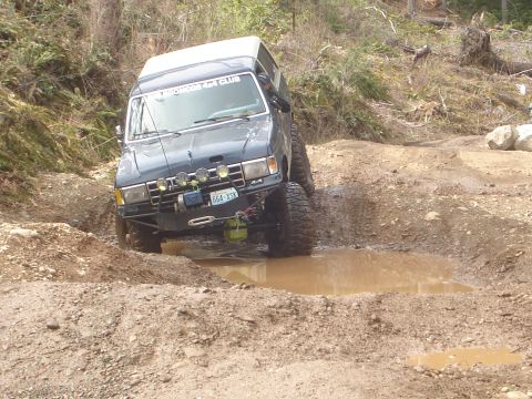 1989 Ford Bronco - Modified 1989 Ford Bronco tackles a challenging muddy obstacle on an off-road trail.