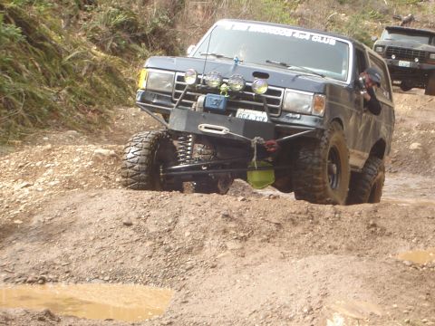 1989 Ford Bronco - This modified SUV is tackling a challenging off-road course with muddy terrain and inclines.