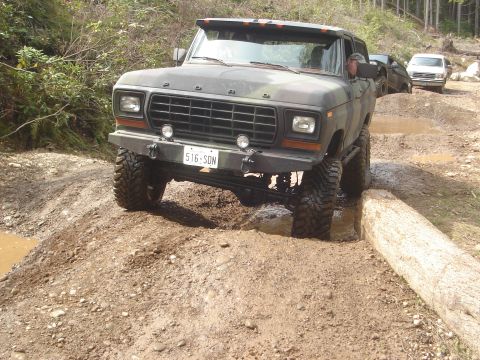 1989 Ford Bronco - This camouflaged 1978 Ford Bronco navigates a muddy off-road course, with another vehicle visible behind it.