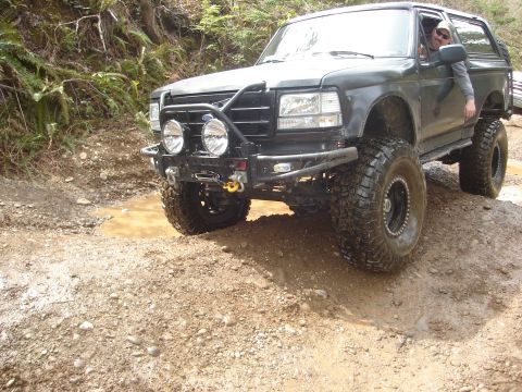 1989 Ford Bronco - This modified SUV navigates a challenging off-road path with deep mud and uneven terrain.