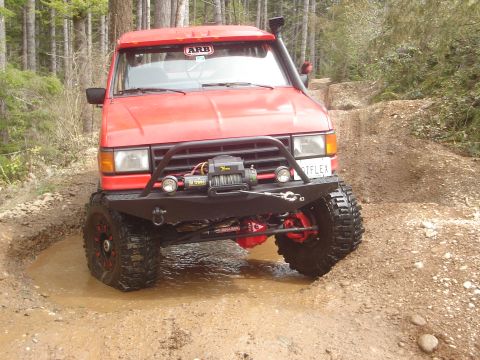 1989 Ford Bronco - This modified off-road vehicle tackles a challenging muddy terrain with its winch and snorkel clearly visible.