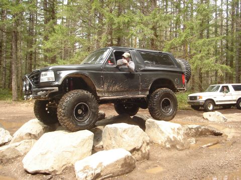 1989 Ford Bronco - A black 1989 Ford Bronco tackles an obstacle course of large rocks, with another Bronco visible in the background.