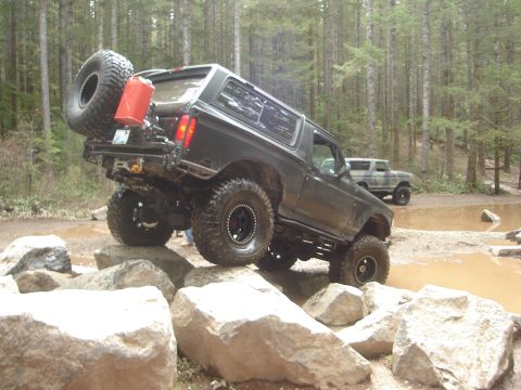 1989 Ford Bronco - Ford Bronco tackling a challenging off-road trail, with another Bronco visible further back.