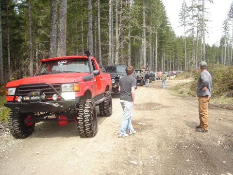 1989 Ford Bronco - A convoy of off-road vehicles are lined up on a dirt road in a forest.