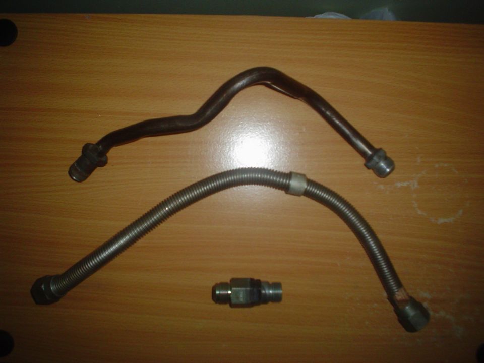 Two metal fuel lines and a connector fitting on a wooden surface