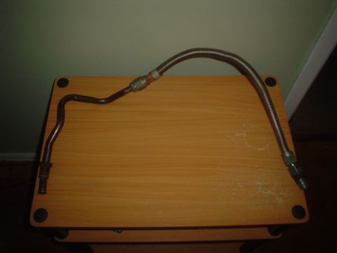 1996 Mercury Grand Marquis - A metal fuel line with a flexible braided section is shown on a wooden surface.