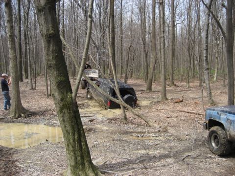 1991 Ford Bronco - Several off-road vehicles are stuck in the mud while navigating a wooded trail.