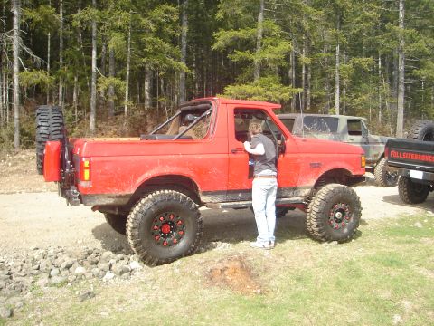 1989 Ford Bronco - Modified red 1989 Ford Bronco parked on a dirt road, with other vehicles visible behind it.