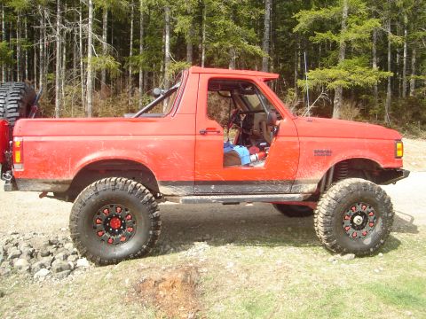 1989 Ford Bronco - This modified red SUV sits in a forest clearing, ready for adventure.