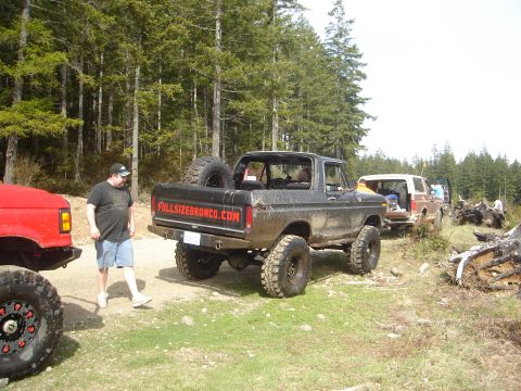 1989 Ford Bronco - A black Ford Bronco is parked off-road with other vehicles nearby.