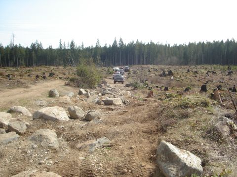 1989 Ford Bronco - A convoy of off-road vehicles navigates a challenging, boulder-strewn trail in a deforested landscape.