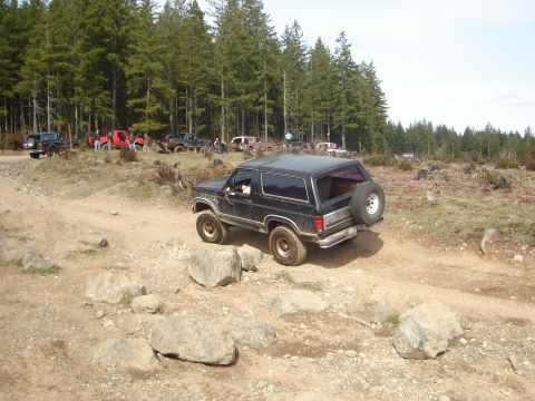1989 Ford Bronco - Several off-road vehicles are gathered in a wooded area with a black Bronco in the foreground.