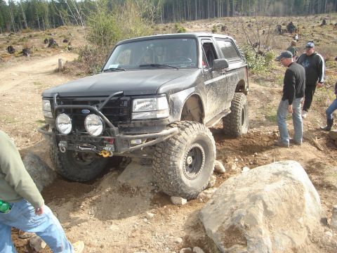 1989 Ford Bronco - Modified 1989 Ford Bronco navigating a rocky, off-road trail with friends watching.