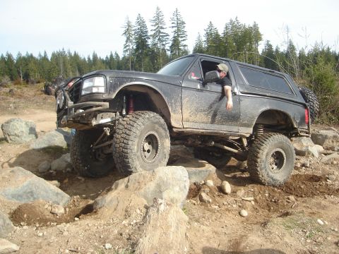 1989 Ford Bronco - A black Ford Bronco navigates a rocky off-road course with a driver inside.