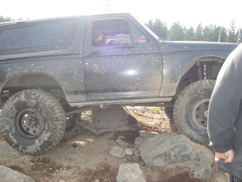 1989 Ford Bronco - A heavily modified Ford Bronco is shown traversing a rocky terrain, with its suspension clearly visible.