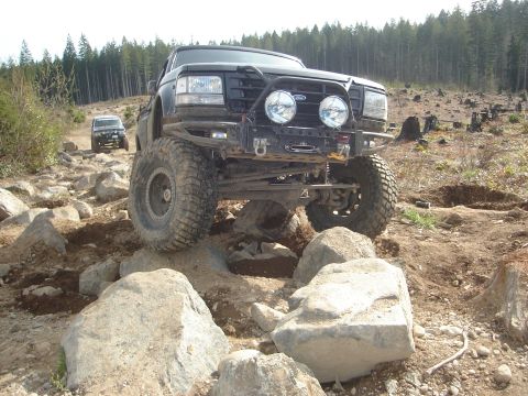 1989 Ford Bronco - A modified black Ford Bronco tackles a rocky trail with another vehicle following behind.
