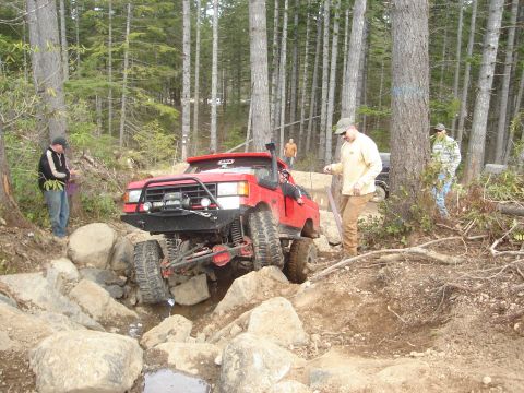 1989 Ford Bronco - A red off-road truck navigates a rocky trail with several people observing the action.