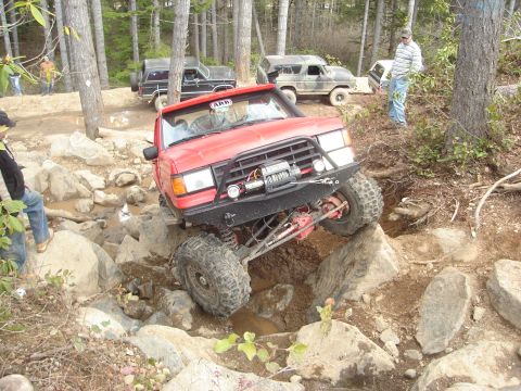 1989 Ford Bronco - Multiple off-road vehicles navigate a rocky trail in a wooded area.