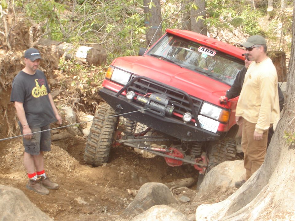 red SUV with winch on front bumper navigating rocky terrain, people watching