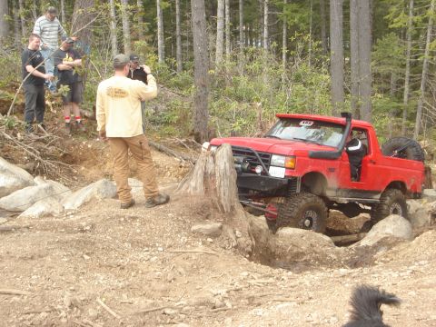 1989 Ford Bronco - A modified red truck tackles a challenging off-road course with onlookers.