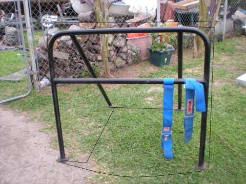1982 Ford Bronco - A roll cage with two blue Simpson racing seatbelts is shown outdoors on a grassy area.