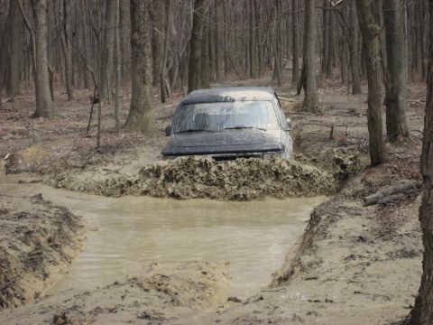 1991 Ford Bronco - A black 1991 Ford Bronco navigates a muddy trail, kicking up water and dirt.