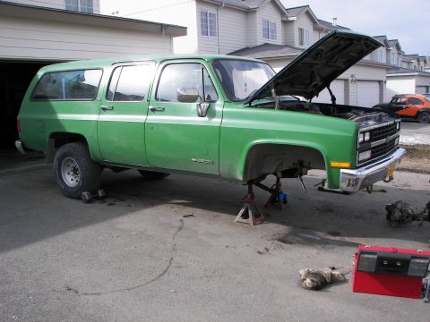 1990 Chevrolet Suburban - This green SUV is on jack stands, undergoing repairs with its front end apart.