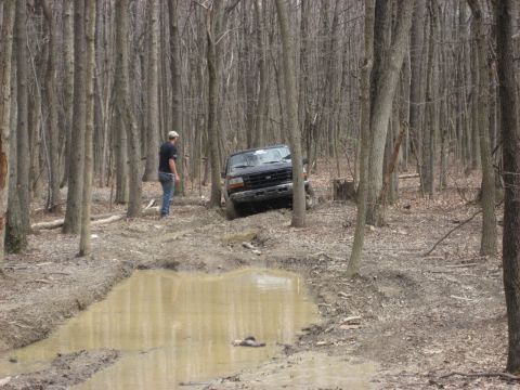 1991 Ford Bronco - A person observes a Ford Bronco navigating a challenging, muddy path through a dense forest.