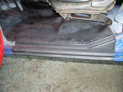 1979 Ford Bronco - The interior floor of a vehicle is visible, with a focus on the driver's side door sill and textured black carpeting.
