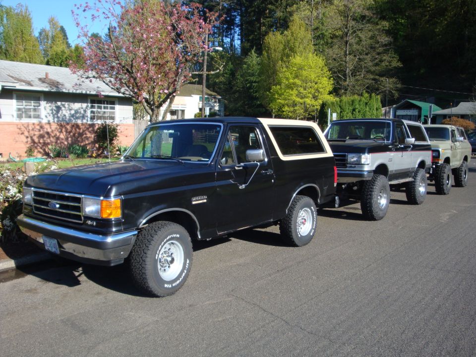Black 1991 Ford Bronco with tan top, parked in a line with other SUVs