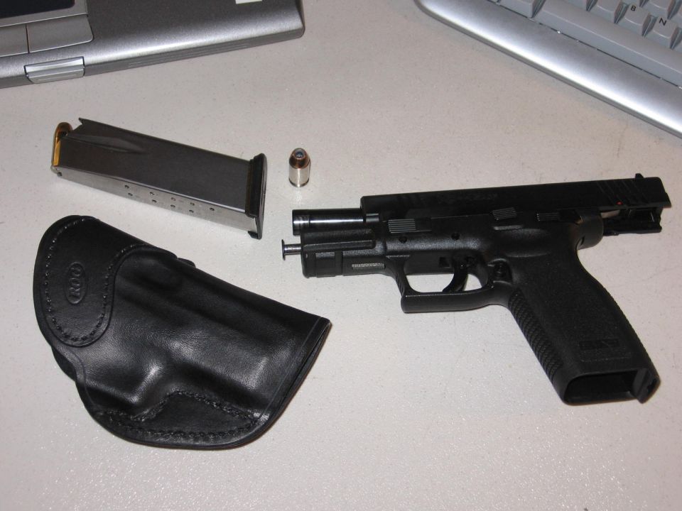 Black semi-automatic pistol with magazine, one cartridge, and leather holster on a white surface