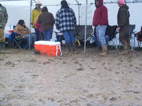 1979 Ford F-250 - A group of people are gathered under a tent in a very muddy outdoor setting.