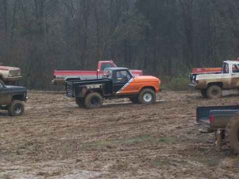 1979 Ford F-250 - Multiple pickup trucks navigate a muddy terrain under overcast skies.