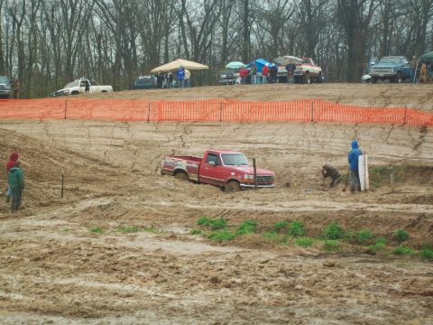 1979 Ford F-250 - A red pickup truck is stuck in the mud at an off-road event, with spectators in the background.